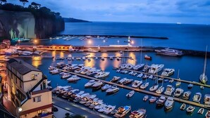 Un puerto deportivo con barcos amarrados, un edificio con balcón y una costa rocosa.