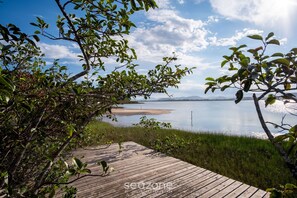 A wooden deck leading to a calm lake with a clear sky. - House w/ BBQ and Lake Access Mat0021 (Garopaba)