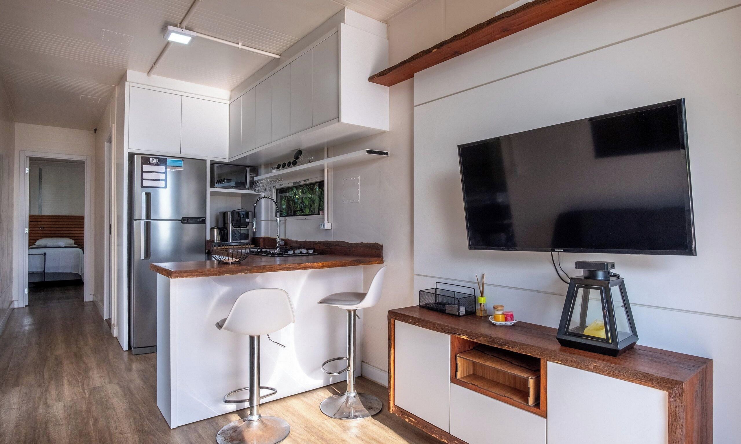 A compact kitchen with a built-in fridge, a microwave, and a gas stove. There is a bar area with two stools and a TV mounted on the wall.