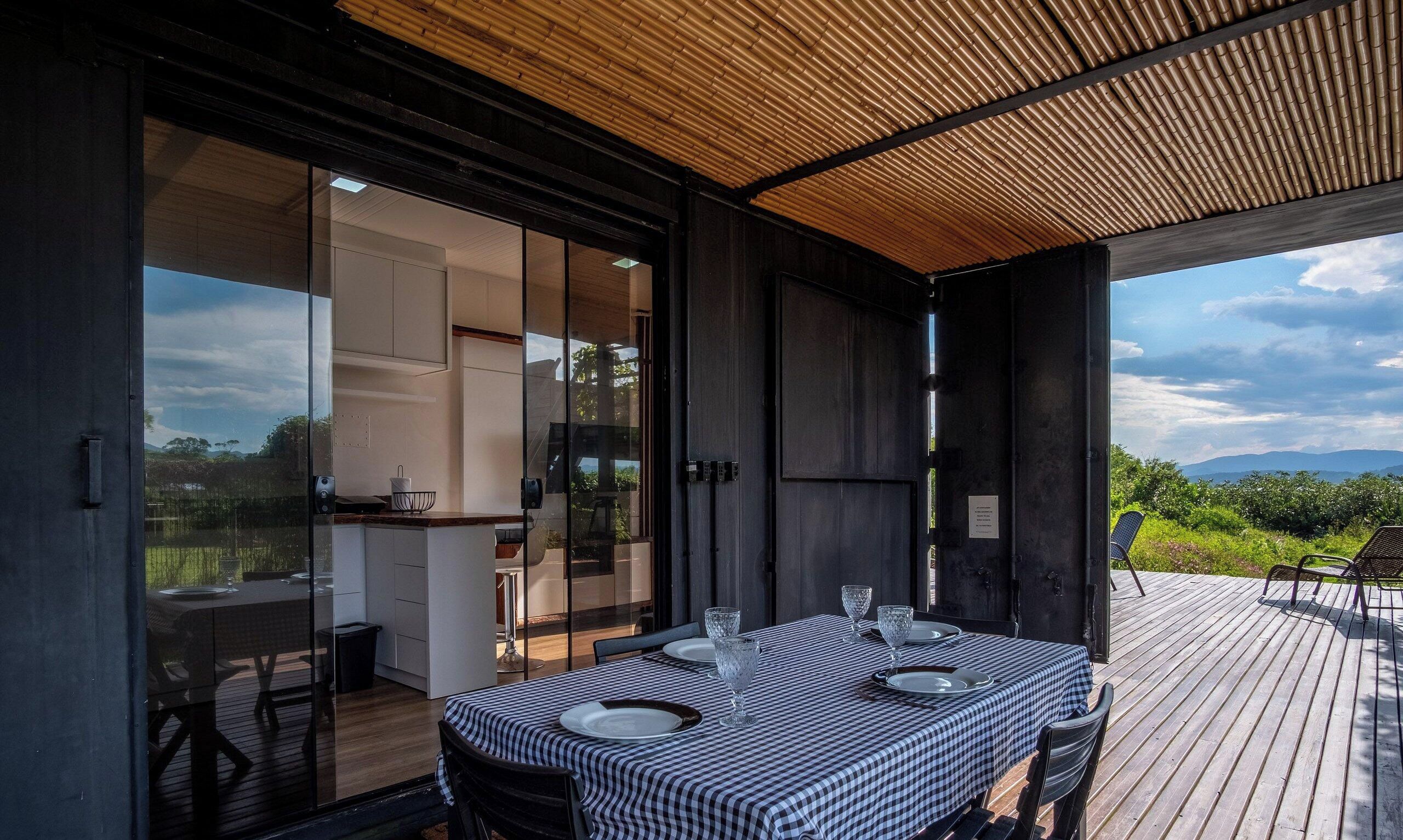 An open-plan kitchen with a dining area on a wooden deck, overlooking a mountainous landscape.