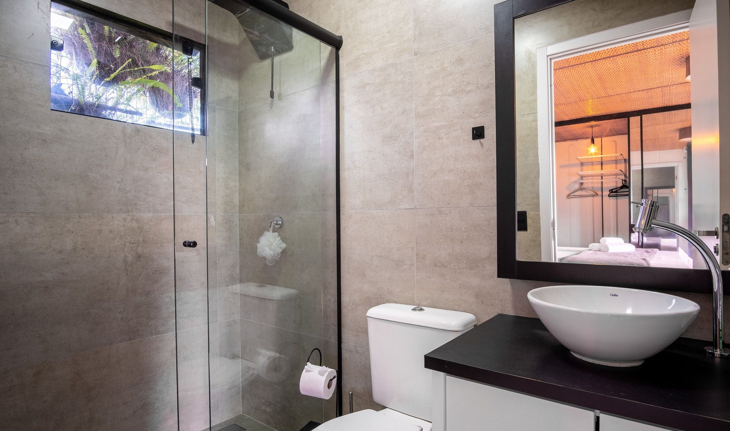 Un baño moderno con cabina de ducha de vidrio, inodoro blanco y un lavabo tipo recipiente grande.