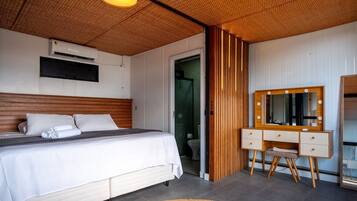 A bedroom with a bed, a vanity with a mirror, and a shower area.