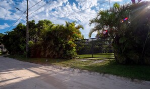 A paved road with a black metal gate, surrounded by lush greenery and palm trees. - House w/ BBQ and Lake Access Mat0021 (Garopaba)