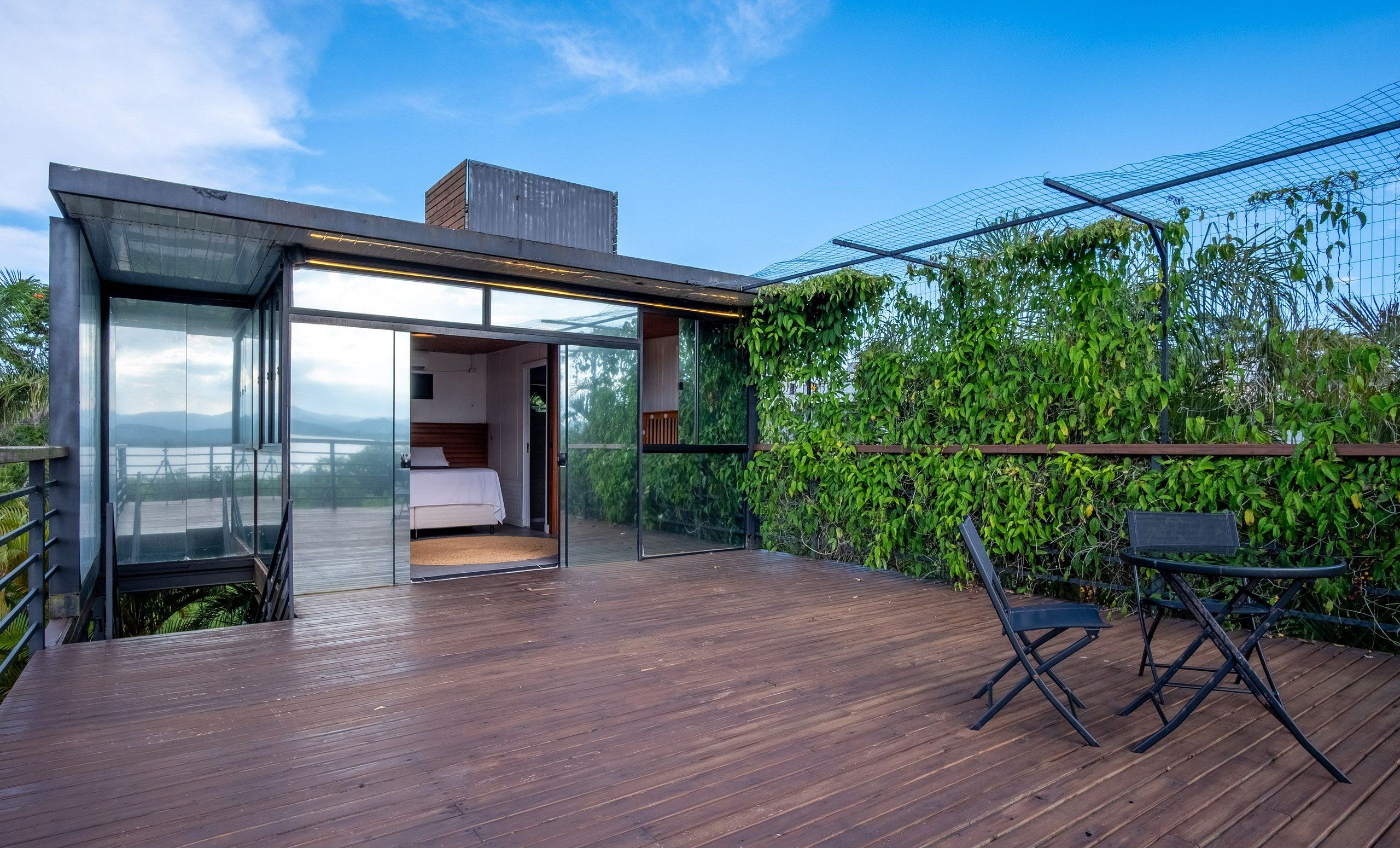 Un dormitorio moderno con paredes de vidrio, terraza de madera y vista al agua.