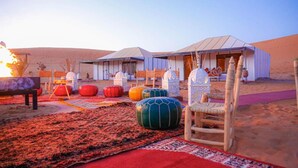 Ein Wüstencamp mit Zelten, bunten Sitzgelegenheiten und einer Feuerstelle.