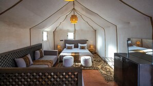 Ein Zelt-Schlafzimmer mit Bett, Sofa, Hocker und Fernseher.