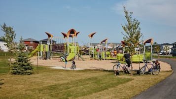 Un parque infantil con varias estructuras de juego, incluyendo toboganes y zonas de escalada, rodeado de césped y árboles.