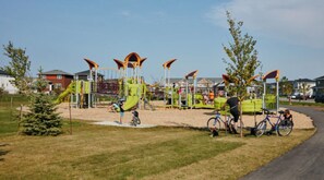 Ein Spielplatz mit verschiedenen Spielgeräten, darunter Rutschen und Kletterbereiche, umgeben von Rasen und Bäumen.