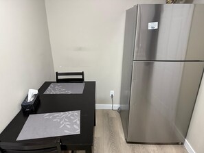 A compact kitchen with a stainless steel refrigerator, a black dining table with two placemats, and a chair.