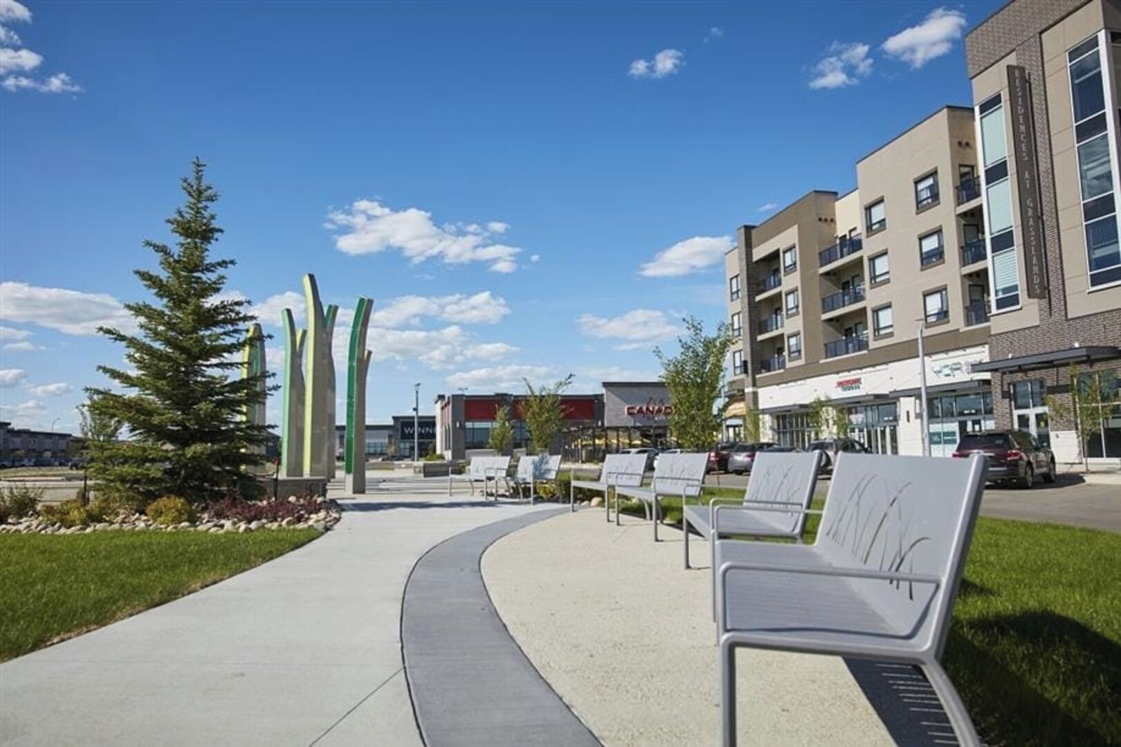 A modern building with a curved walkway, outdoor seating, and a clear sky.