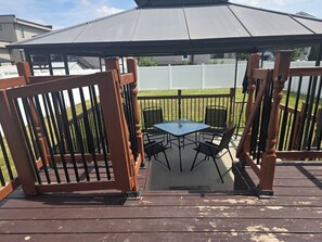 Ein überdachter Patio-Bereich mit Tisch und Stühlen, umgeben von einer Holzterrasse und Metallgeländern.