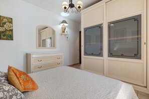 A bedroom with a bed, a dresser, a mirror, a chandelier, and a wardrobe. - Holiday Home 'Fiorita' with Wi-Fi and Air Conditioning (Budoni)