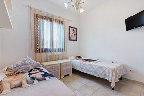 Un dormitorio con dos camas, una ventana con cortinas, un cuadro en la pared y un televisor montado en la pared.