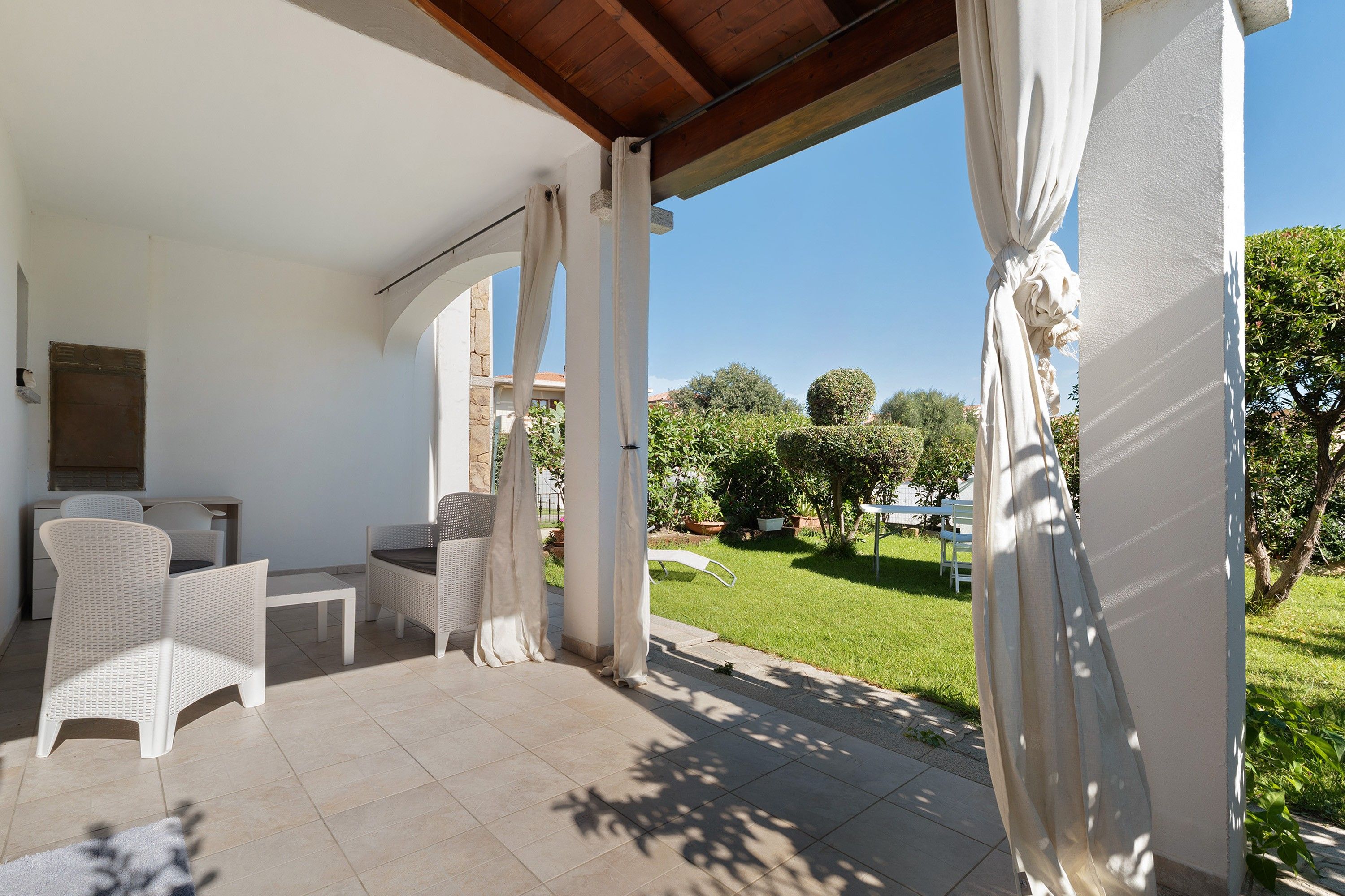Ein überdachter Patio-Bereich mit weißen Korbmöbeln, einem Tisch und Stühlen.