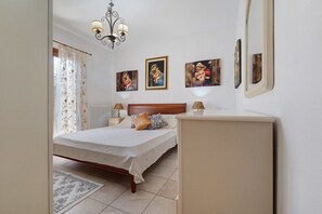 Une chambre à coucher comprenant un lit, des tables de chevet, une commode, un lustre et des œuvres d’art murales.