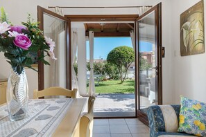 Une terrasse ouverte avec une table à manger, des chaises, un canapé et une vue sur un jardin et des bâtiments.
