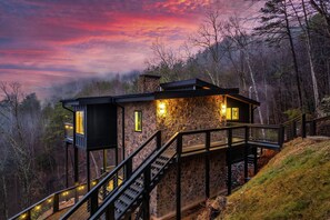 Eine Steinhütte mit einer Holzterrasse und Treppe, umgeben von Bäumen.