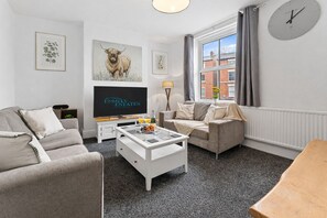 Ein modernes Wohnzimmer mit Sofa, Sesseln, Couchtisch und Flachbildfernseher.