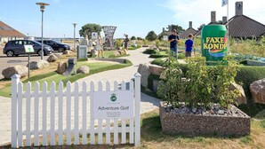A golf course entrance with a white picket fence, a sign for 'Adventure Golf', and a large can of Faxe Kondi. - 2 Rooms, Standard, 2+2 People, 48m2 (Karrebæksminde)