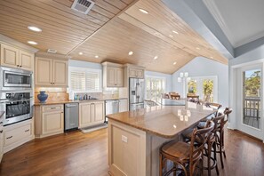 A spacious kitchen with wooden cabinets, a large island with bar stools, stainless steel appliances, and a view to the outside. - 360 Views, Rooftop Deck, Across from Beach Access - 413 Tarpon Blvd (Fripp Island)
