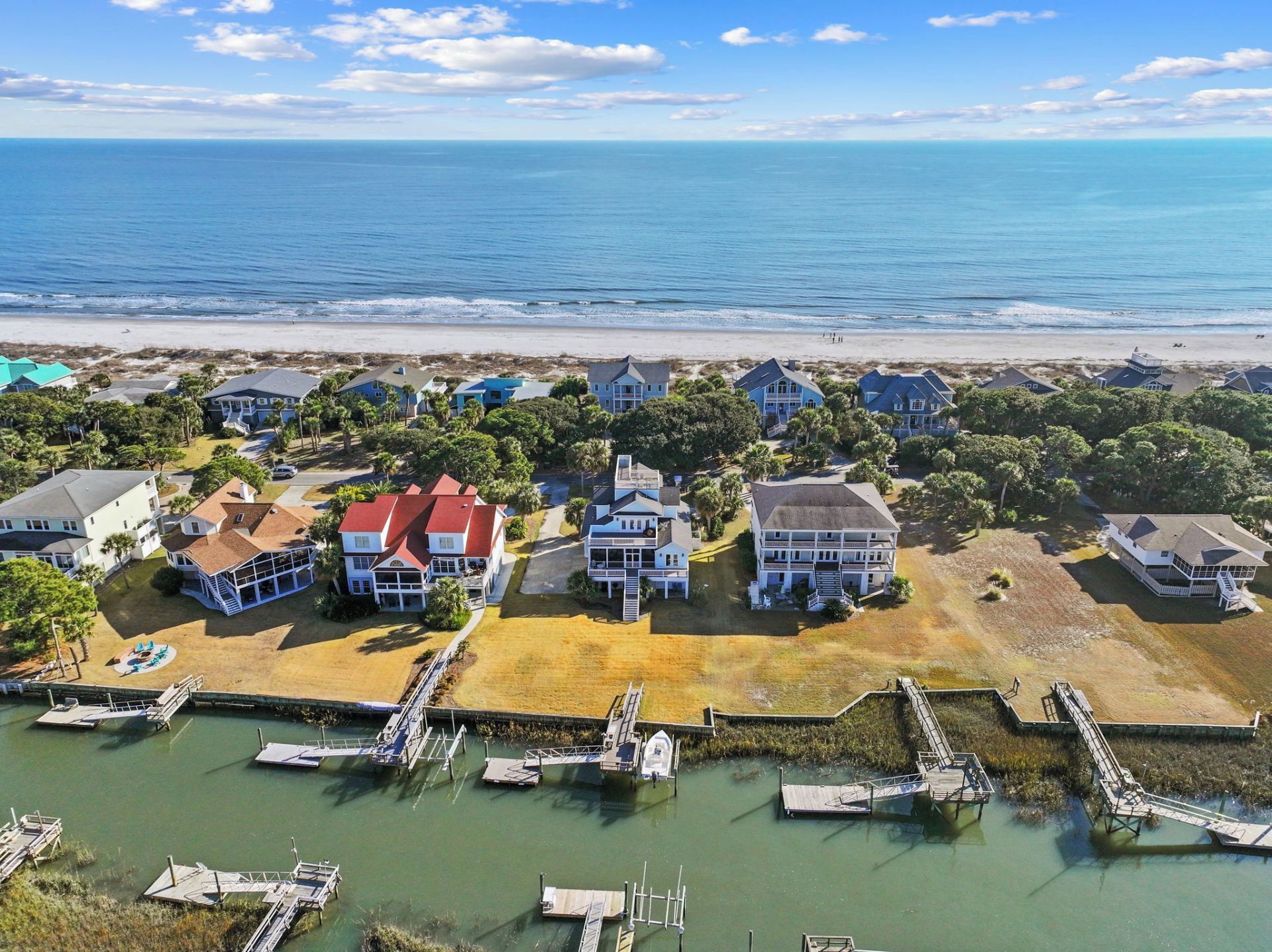 An aerial view of a coastal residential area with multiple houses, a marina, and a beach in the background.