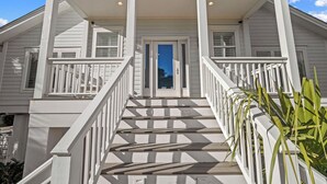 Ein zweistöckiges Haus mit Veranda, einer Treppe mit weißen Geländern und einer Tür mit Glasfeldern.