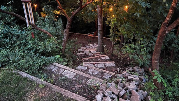 Un sendero de madera que atraviesa un jardín con árboles y luces colgantes.