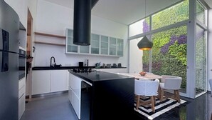 Une cuisine moderne dotée d’un grand îlot central, de meubles blancs et offrant une vue sur la verdure grâce à de grandes fenêtres.