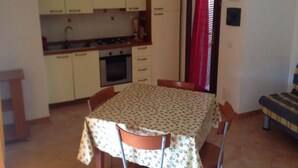 A compact kitchen with a dining table and chairs, a small oven, and a refrigerator. - Charming Family Villa With Pool (Trinità d'Agultu e Vignola)
