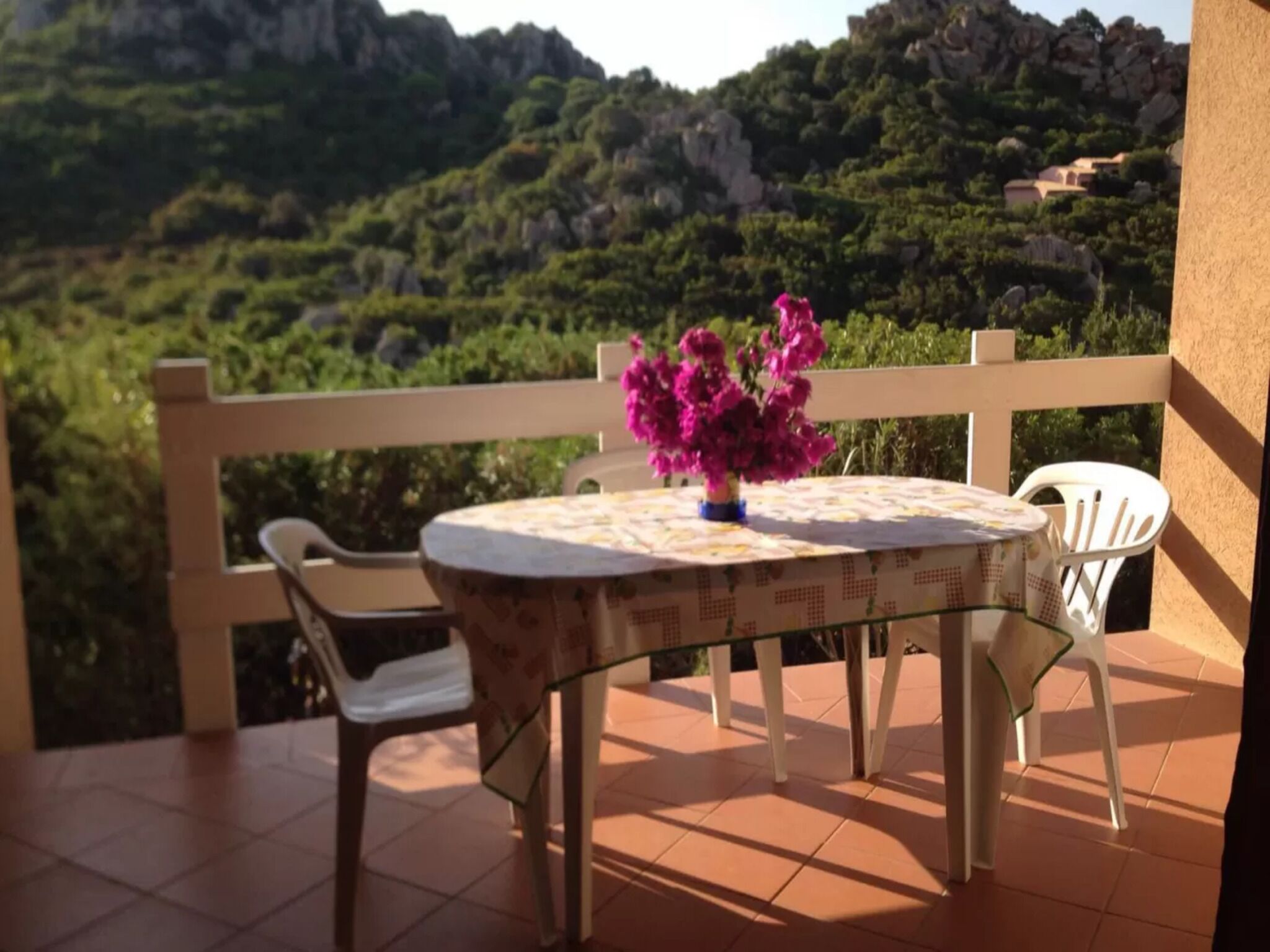 Ein Balkon mit Tisch und Stühlen, einer Blumenvase und Blick auf eine gebirgige Landschaft.
