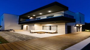 Ein modernes, zweistöckiges Haus mit einer Holzterrasse und einer Sitzgelegenheit im Freien.