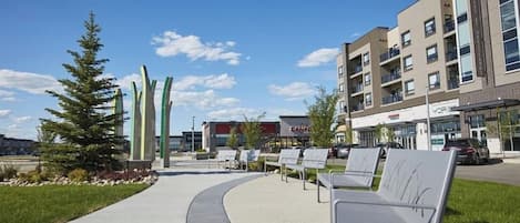 A modern building with a curved walkway, outdoor seating, and a clear sky.