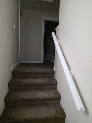 Eine Teppichstufen Treppe mit weißen Geländern, die zu einer Tür hinaufführt.