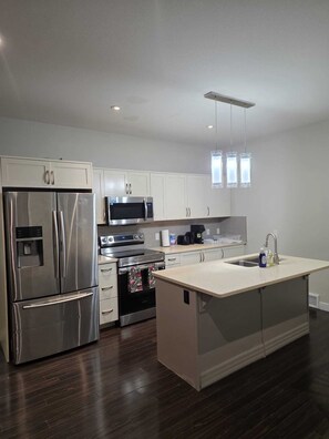 A modern kitchen with stainless steel appliances, white cabinetry, and a central island with a sink. - Home away from home (Regina)