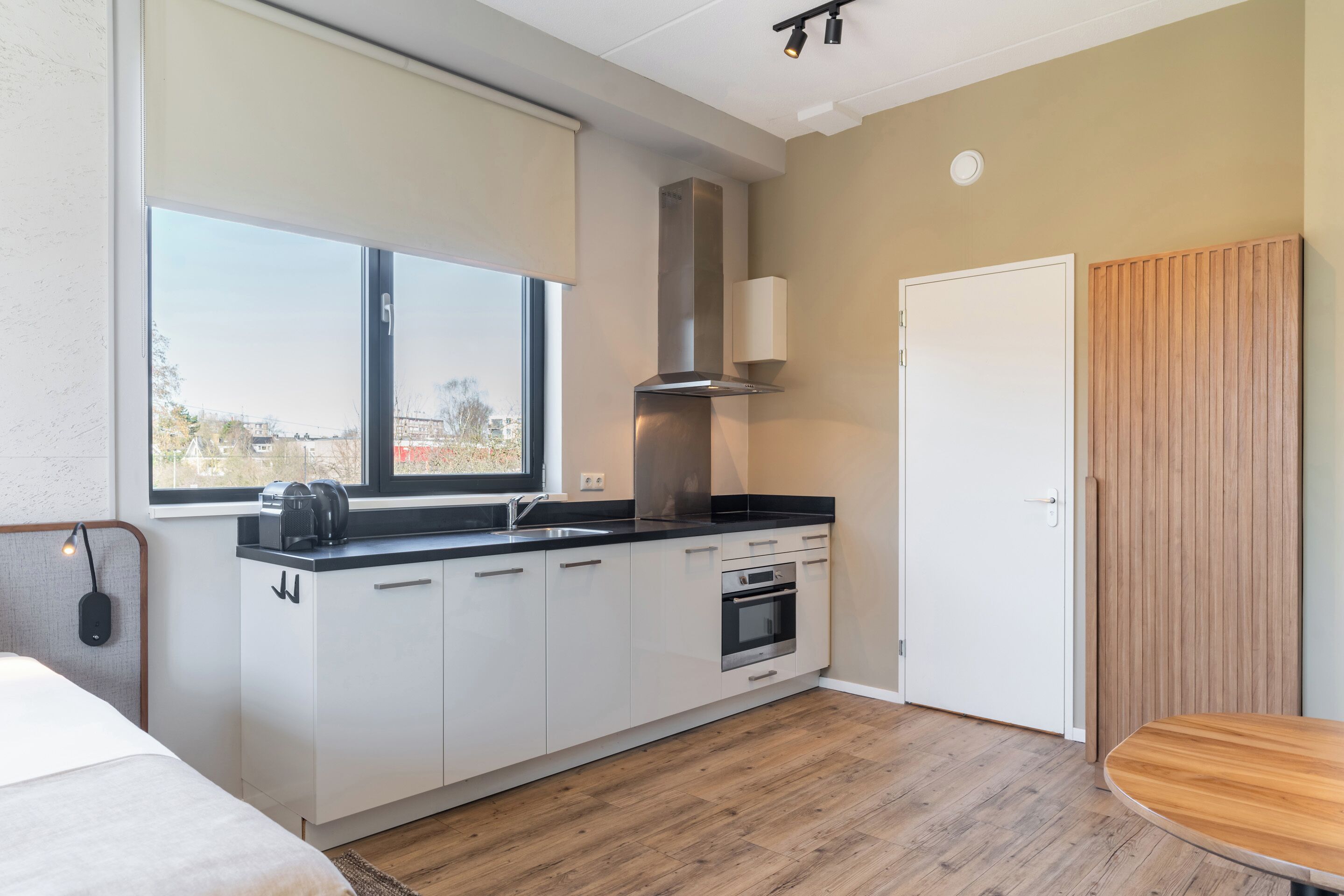 A modern kitchen with a large window, a built-in oven, and a wooden door.