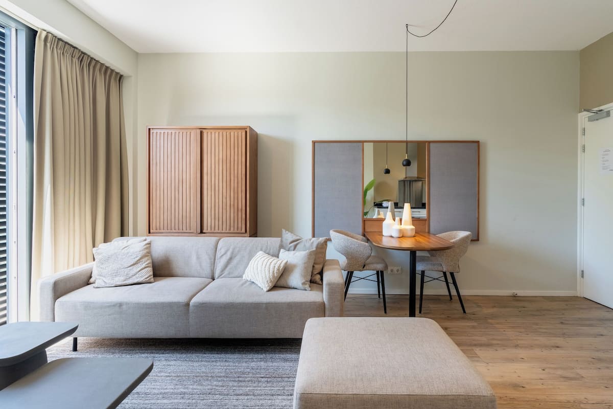 A modern living room with a sofa, ottoman, and dining area.