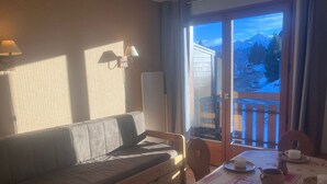 Ett mysigt rum med en soffa, ett matbord dukat för te och en utsikt över ett snöigt berglandskap genom fönstret.