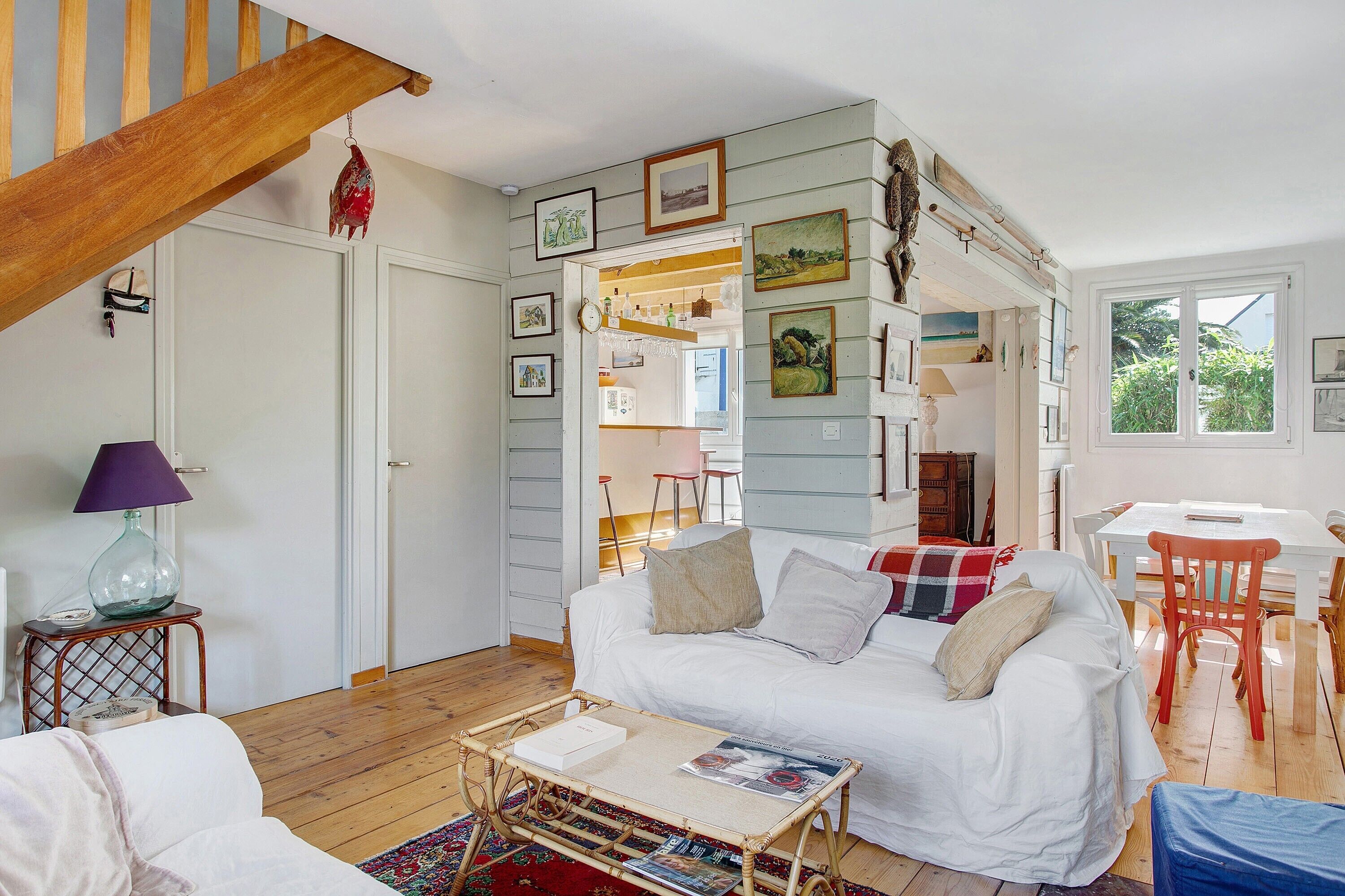 A cozy room with a wooden staircase, a white sofa, a small table, and a dining area with a white table and red chairs.