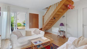 Een woonkamer met een houten trap, witte meubels en uitzicht door een glazen deur.