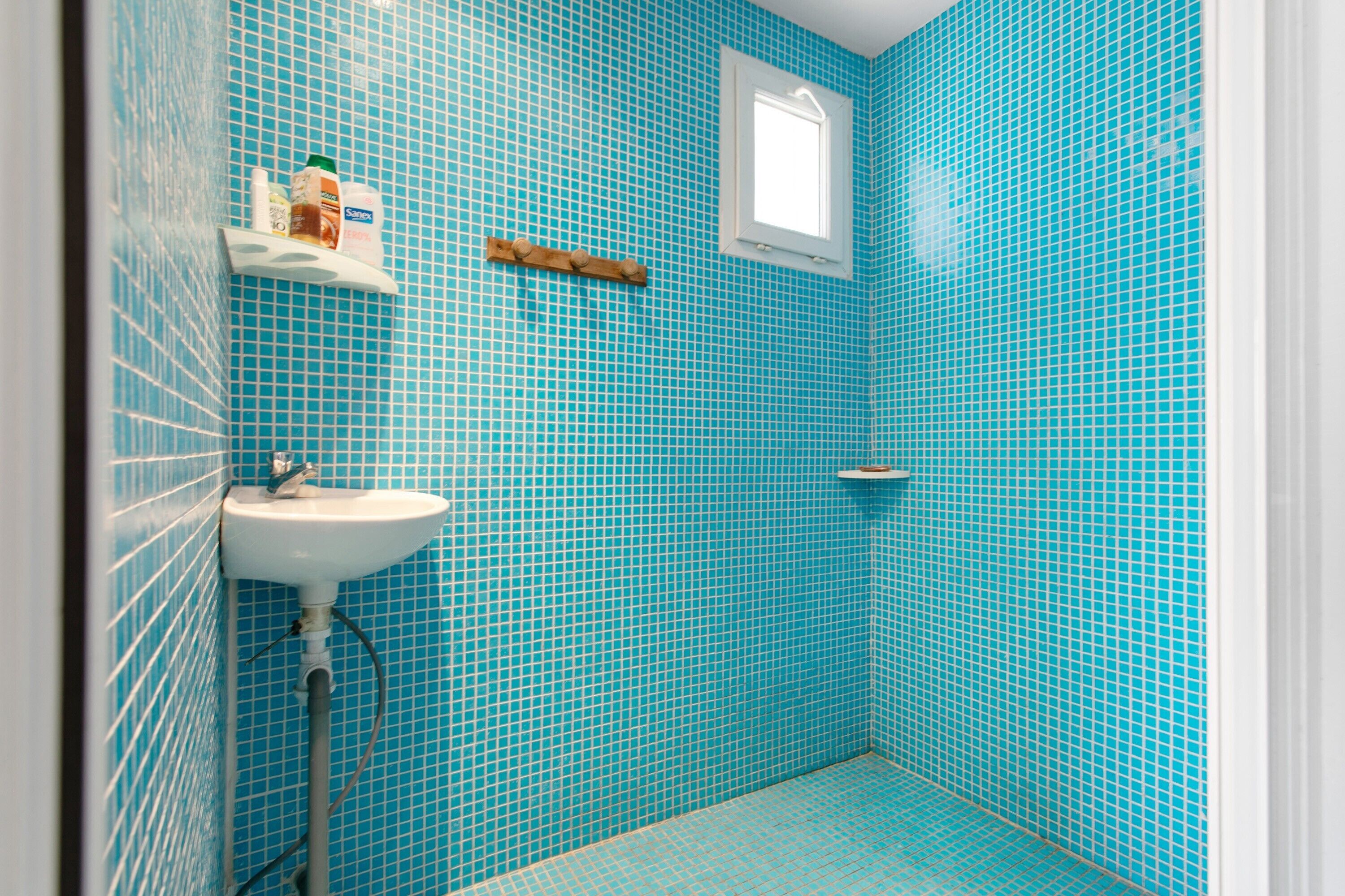 Un bagno con un lavandino, una finestra e uno scaffale con articoli da toilette.
