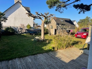 A wooden deck, a garden, a house, and a red car. - Spacious house in Locquirec with terrace, 300m from the beach (Locquirec)
