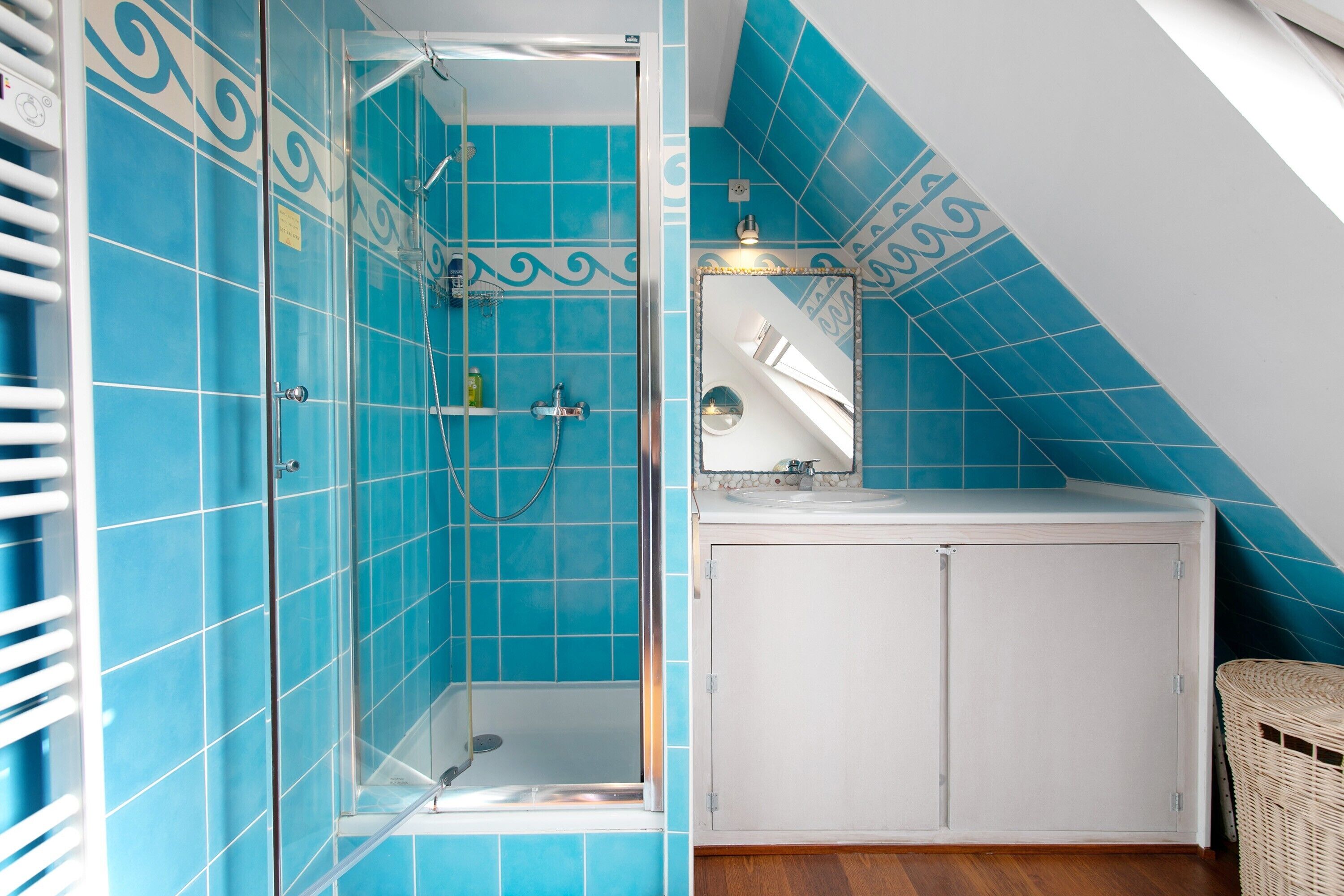 Un baño con azulejos azules, una cabina de ducha de vidrio, un lavamanos blanco y un espejo.