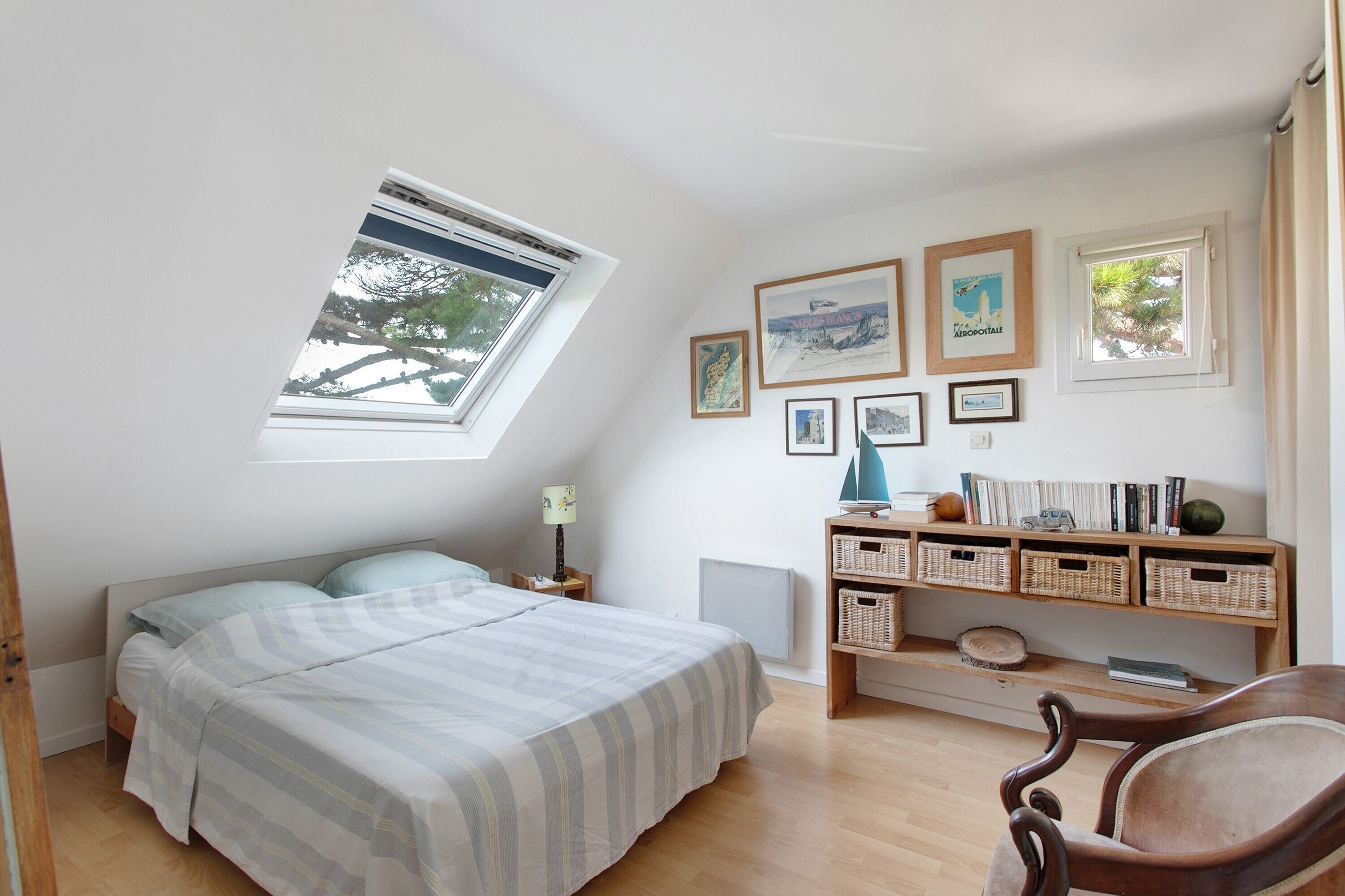 A bedroom with a bed, a desk with a chair, a window, and wall-mounted artwork.