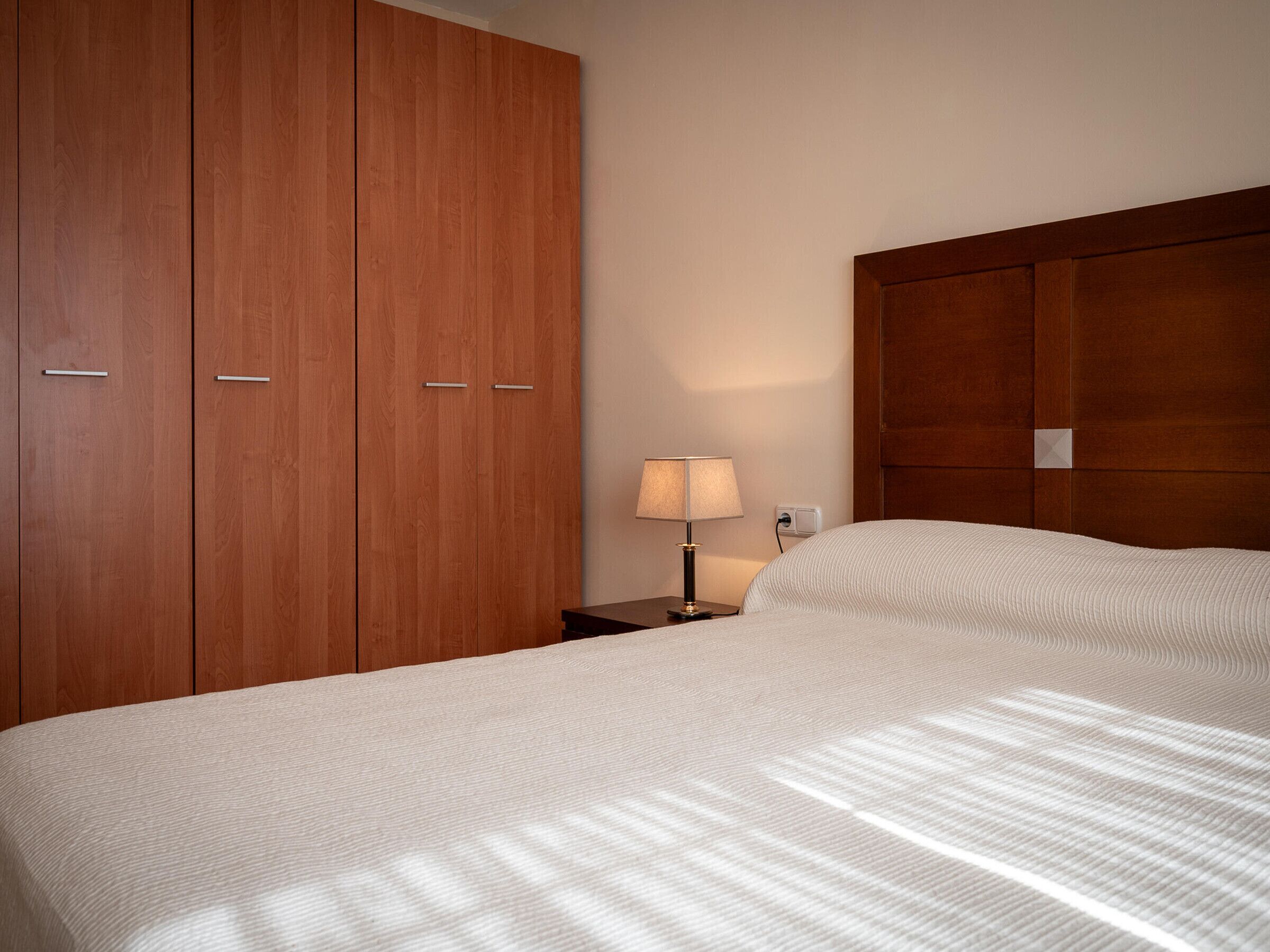 Een hotelkamer met een grote houten garderobe, een nachtkastje met een lamp en een opgemaakt bed.
