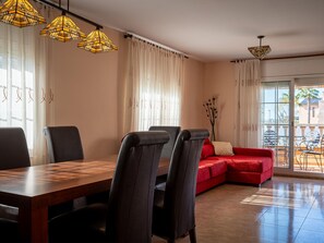 A dining area with a wooden table and chairs, a red sofa, and a balcony with outdoor furniture. - 4-Bedroom Townhouse, Air-Conditioned, Near Beach (Creixell)