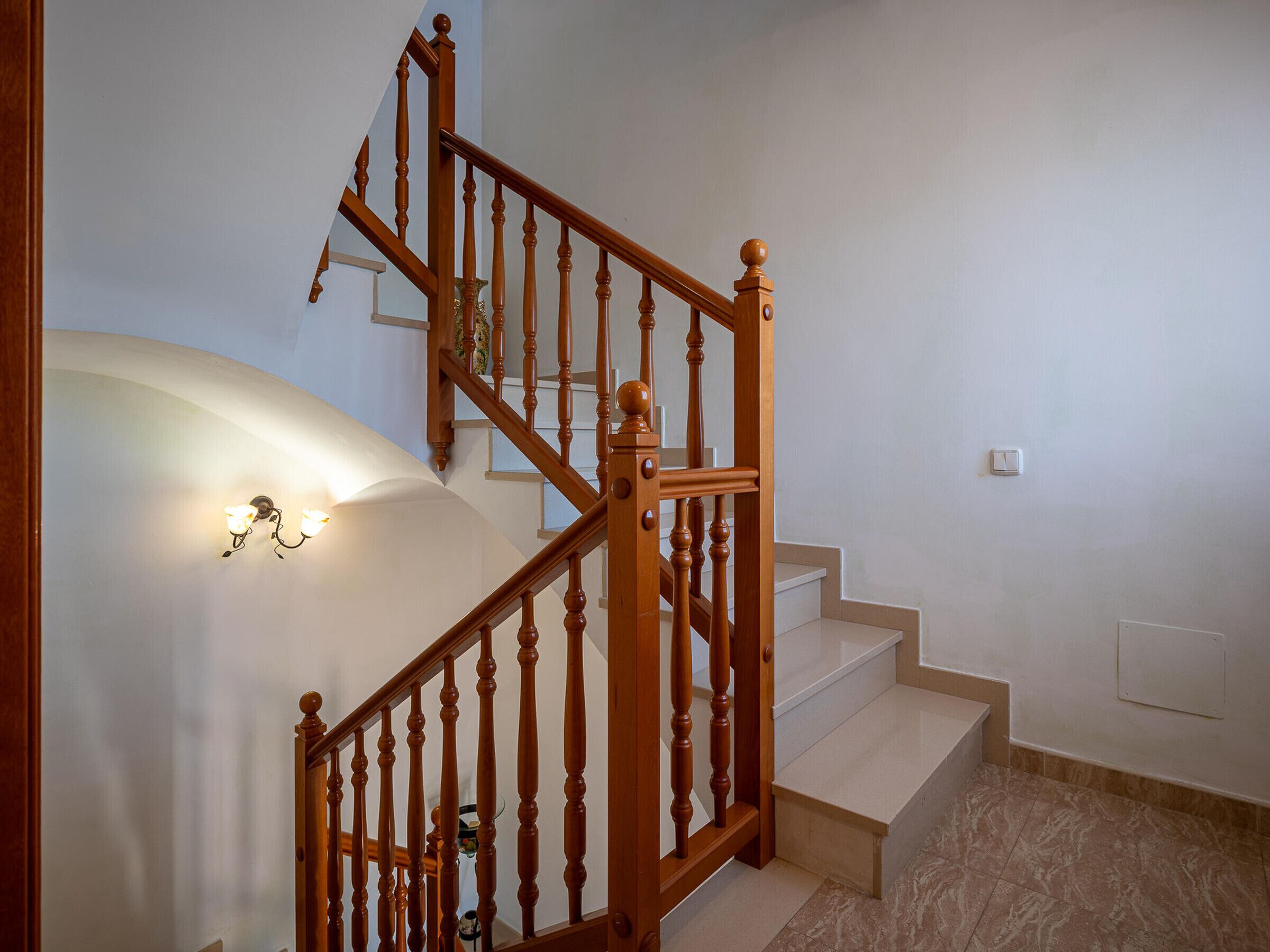 A wooden staircase with a handrail, a light fixture on the wall, and a power outlet on the wall.