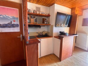 Una cocina compacta con armarios de madera, microondas integrado y un refrigerador pequeño.