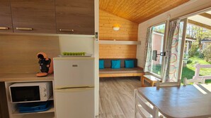A compact kitchen with wooden cabinets, a microwave, and a refrigerator. There is a small seating area with cushions and a view of the outdoors. - Cozy Chalet for 5 with Terrace (Montlaur)