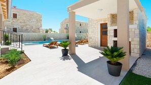 Un'area esterna moderna con piscina, edifici in pietra e poltrone relax.