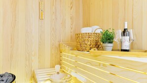 Una sauna in legno con panche, un cesto intrecciato, una pianta in vaso e una bottiglia di vino con i bicchieri.